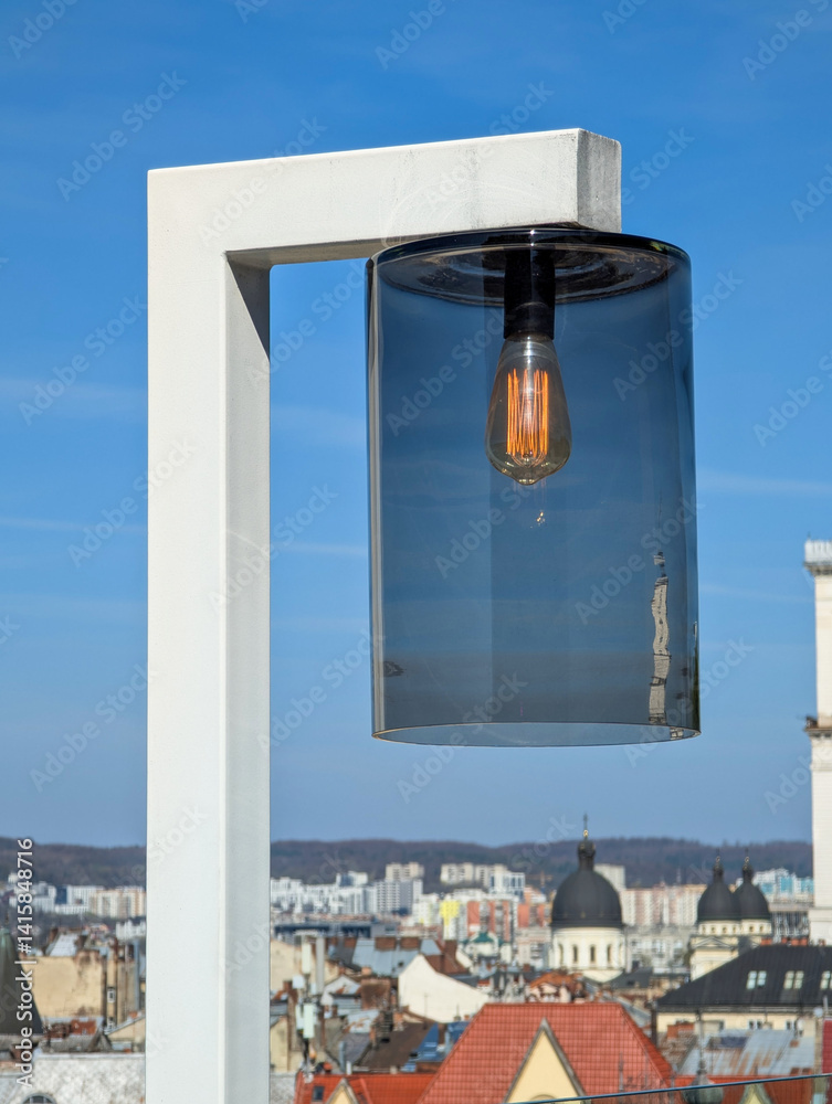 Modern lamp with glass shade against clear blue sky.