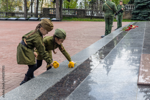 Patriotic education. Little girls in military uniform laying flowers at the eternal flame near the monument to fallen soldiers in world War II. Victory Day on May 9 photo