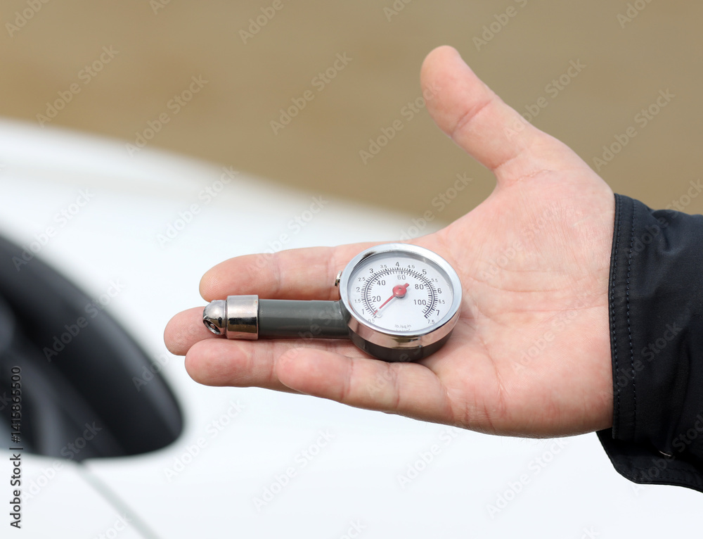 Close-up of a hand holding an analog tire pressure gauge, with a clear dial showing psi and kPa readings, against the backdrop of a white vehicle, emphasizing car maintenance and safety awareness. Close-up of a hand holding an analog tire pressure gauge, with a clear dial showing psi and kPa readings, against the backdrop of a white vehicle, emphasizing car maintenance and safety awareness.