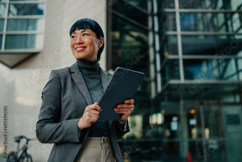 Bild auf Leinwand Smiling businesswoman holding tablet and looking away outside office building