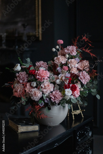 Luxurious bouquet of preserved flowers with roses on black table and dark background.