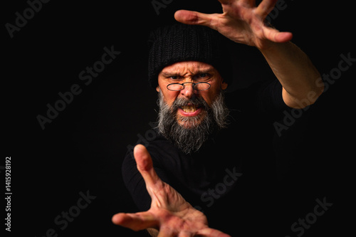 Dramatic portrait of an energetic man with a beard and glasses reaching out to the camera, trying to take it with his hands. Subtle lighting, emotional expression, dark background, mysterious concept