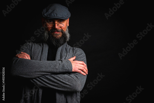 Obraz na płótnie emotional, macro portrait of a serious bearded man in a cap and glasses on a black background. Stylish, intense look with a confident and mysterious expression, emotions place for inscription on a bil w salonie