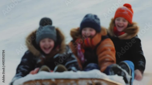 Three children, bundled in warm winter clothing, smile widely as they sled down a snowy hill. The setting sun casts a golden hue, illuminating their joyful faces and the sparkling snow around them.