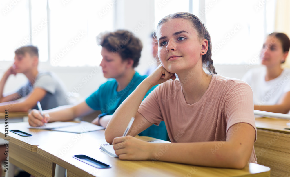 Teenager students sitting at desks and listening. Girl sitting in foreground and smiling.