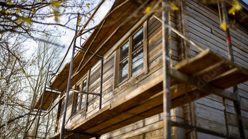 Exterior view of a wood paneled house with visible windows and scaffolding suggesting a renovation or building construction project.