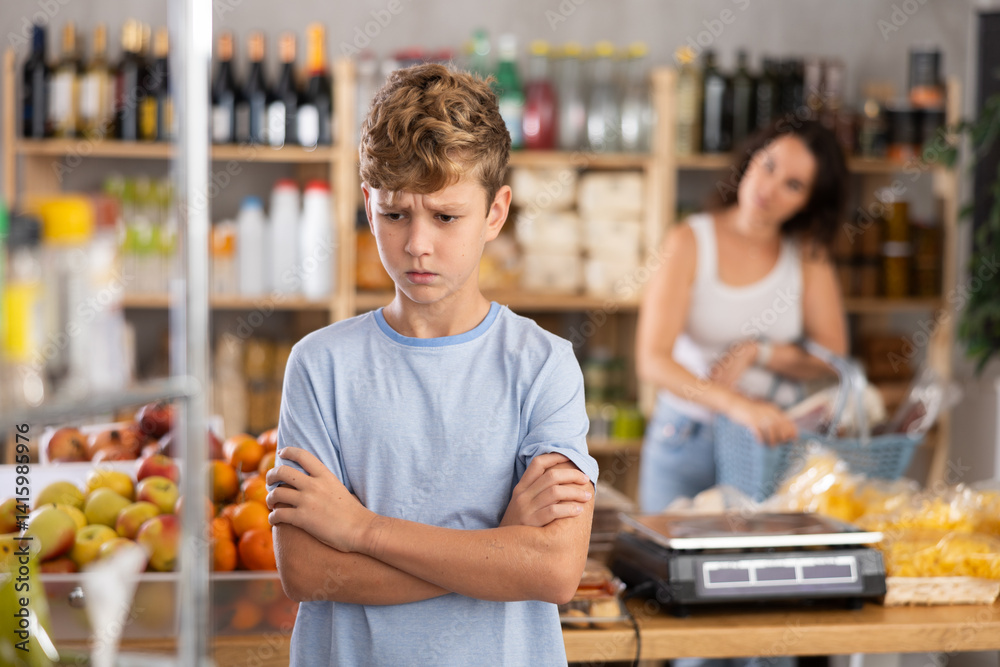 Sad and angry boy stands near window of candy store. Disgruntled mother screams and scolds boy, reproaches him. Mom scolds boy, does not allow him to buy sweets Sad and angry boy stands near window of candy store. Disgruntled mother screams and scolds boy, reproaches him. Mom scolds boy, does not allow him to buy sweets