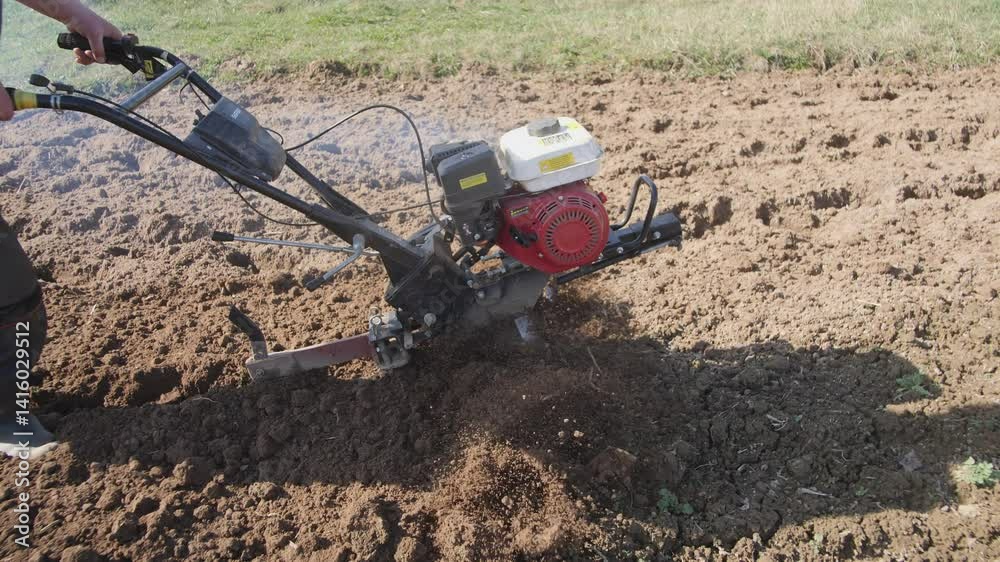 An individual is using a rototiller on dry earth, preparing the ground for future planting and gardening An individual is using a rototiller on dry earth, preparing the ground for future planting and gardening
