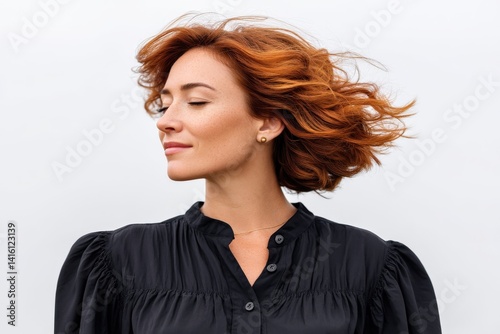 Redheaded woman in black shirt turning head with hair in motion and eyes closed in side view against sky blue background expressing emotional liberation serenity and individuality