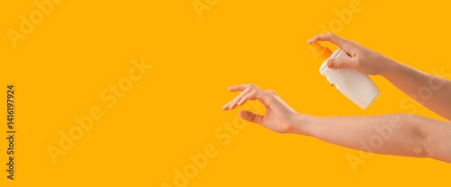 Hands of woman applying sunscreen cream on yellow background with space for text