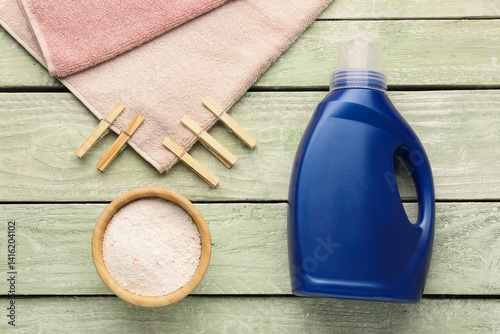 Laundry detergents, clothespins and towel on green wooden background