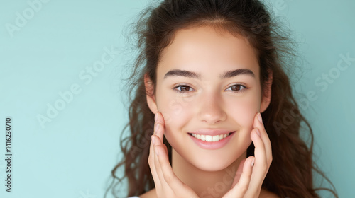 Young woman smiling while touching her face against a light blue background, showcasing a natural skincare routine during the day.