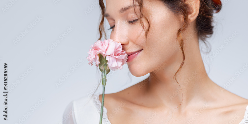 A serene portrait of a woman gently sniffing a soft pink flower with her eyes closed. The clean, minimalistic background enhances the peaceful and graceful mood. Ideal for themes related to beauty