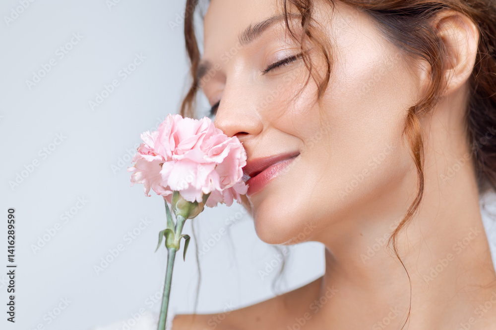 Fototapeta premium Close-up of a joyful Caucasian woman with radiant skin and natural makeup gently smelling a pink carnation. Ideal for fragrance, skincare, floral beauty, and feminine wellness campaigns.