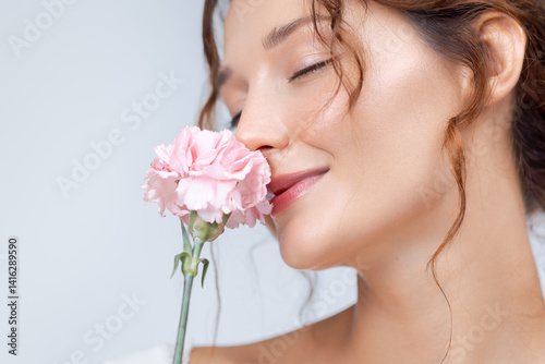 Close-up of a joyful Caucasian woman with radiant skin and natural makeup gently smelling a pink carnation. Ideal for fragrance, skincare, floral beauty, and feminine wellness campaigns.