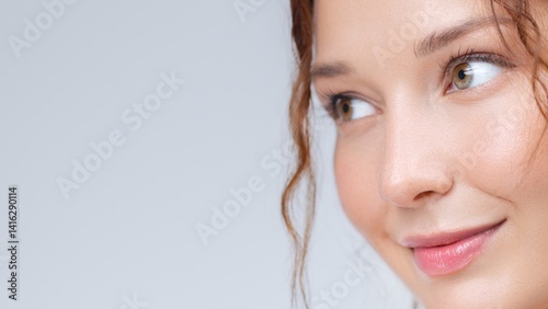 Beautiful young woman with clear glowing skin and glossy lips looks to the side with a gentle smile. Ideal for skincare, beauty, wellness, and natural cosmetics branding concepts.