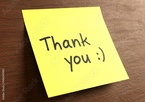 Bright yellow sticky note with handwritten message of appreciation placed on a wooden desk