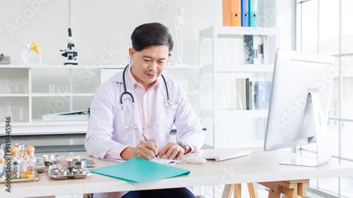 Obraz na płótnie Portrait of asian doctor positive confident consulting sitting at desk working physician wearing stethoscope in clinic hospital using computer writing in notepad online research medical for wellness. w salonie