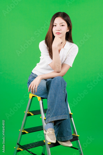 Portrait of asian beautiful young woman long hair, female model smile confident wear white shirt and blue jean look at camera sitting on stairs in green background studio. Fashion lifestyle concept.