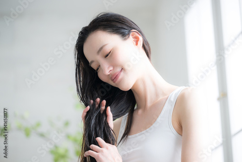 若い女性の濡れた髪のヘアオイルを塗るトリートメント　毛先の枝毛などをケアするイメージ photo