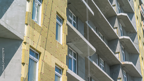 Construction work on the exterior cladding of the building. Laying of thermal insulation material on the walls. Insulation of the house. Plastering the walls. Balconies of a house under construction.