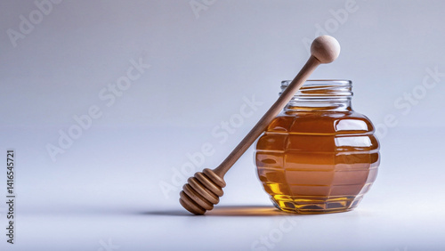 Glass jar filled with rich golden honey with  wooden honey dipper on  gray background