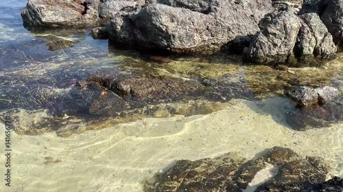 Repeat ripple wave of sea attack to stones with sunny reflection. Sand beach under clear water of sea. 