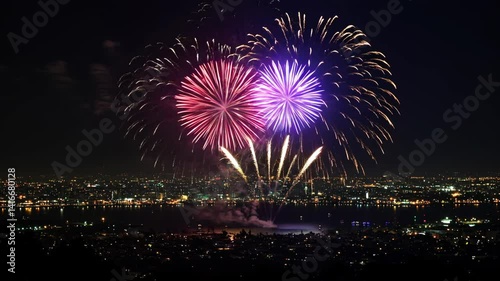 Beautiful multi colored fireworks bursting over a well lit cityscape background at night with the lights reflecting off the river water in the foreground