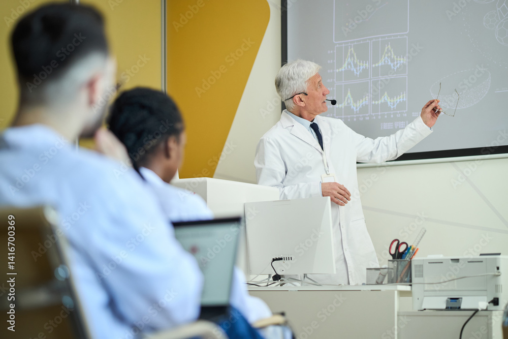Obraz premium Senior scientist giving lecture in modern classroom using screen and technology while diverse audience attentively listening and taking notes