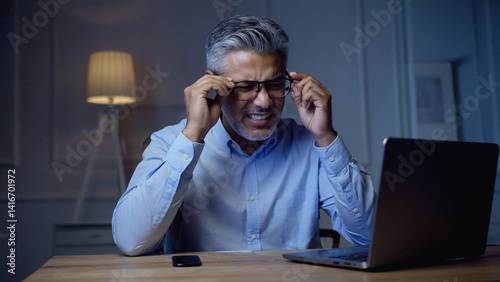 Weary Reflections: A professional, eyes weary, struggles to maintain focus, conveying the strains of working late, under the soft, artificial glow of a desk lamp.