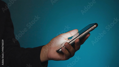 Digital Connection: A close-up shot reveals a hand delicately cradling a modern smartphone, its screen emitting a soft, cool light that reflects on the person's skin, set against a deep blue backdrop.