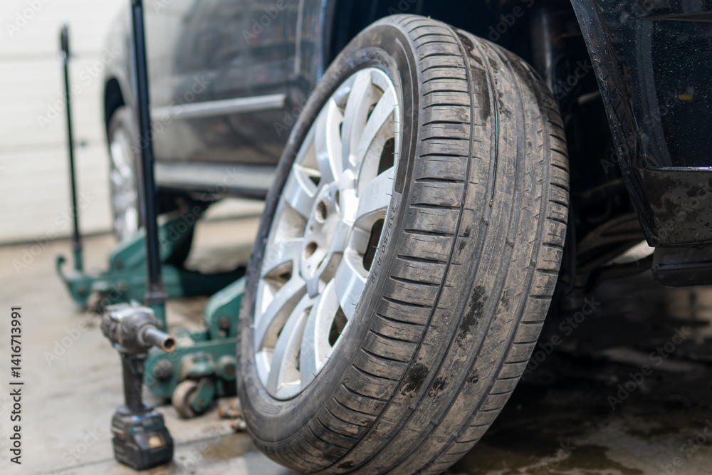 Car Tire Change Process with Vehicle Lifted on Jack During Seasonal Maintenance. Close-up of Tire on Alloy Wheel Being Removed or Installed with Professional Hydraulic Equipment Visible in Background Car Tire Change Process with Vehicle Lifted on Jack During Seasonal Maintenance. Close-up of Tire on Alloy Wheel Being Removed or Installed with Professional Hydraulic Equipment Visible in Background