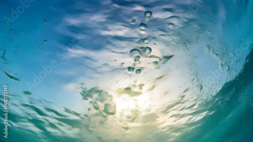 Bubbles rising to the top of water waves as sun light shines through the blue water surface