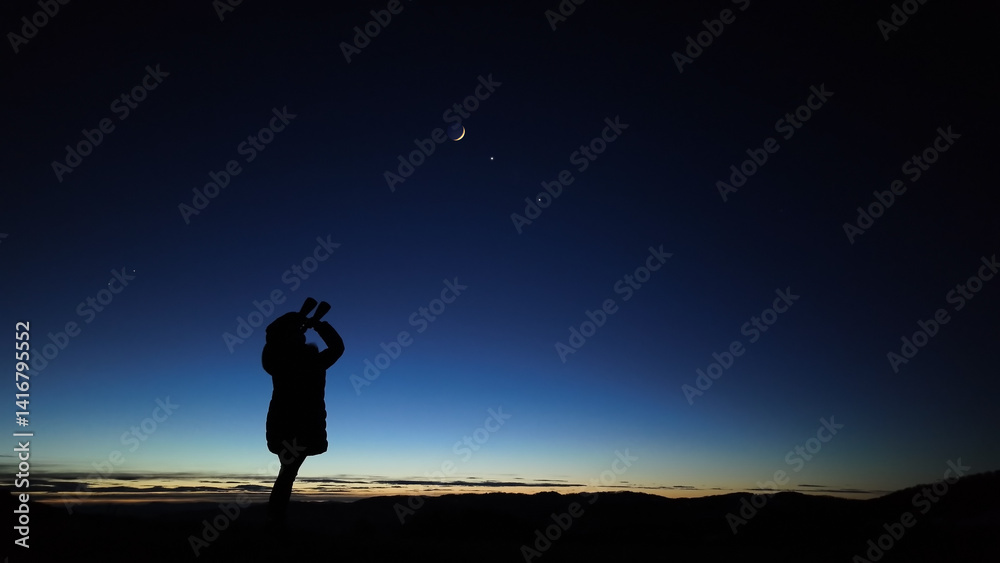 Amateur astronomer looking at the evening skies, observing planets, stars, Moon and other celestial objects with binoculars.