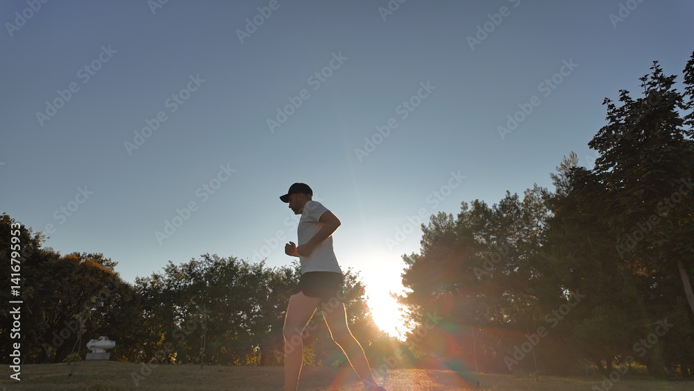 Man exercising and jogging in a park during summertime golden hour time.