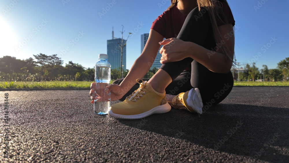 Young attractive sporty woman making pause for drinking water during exercising in the park.
