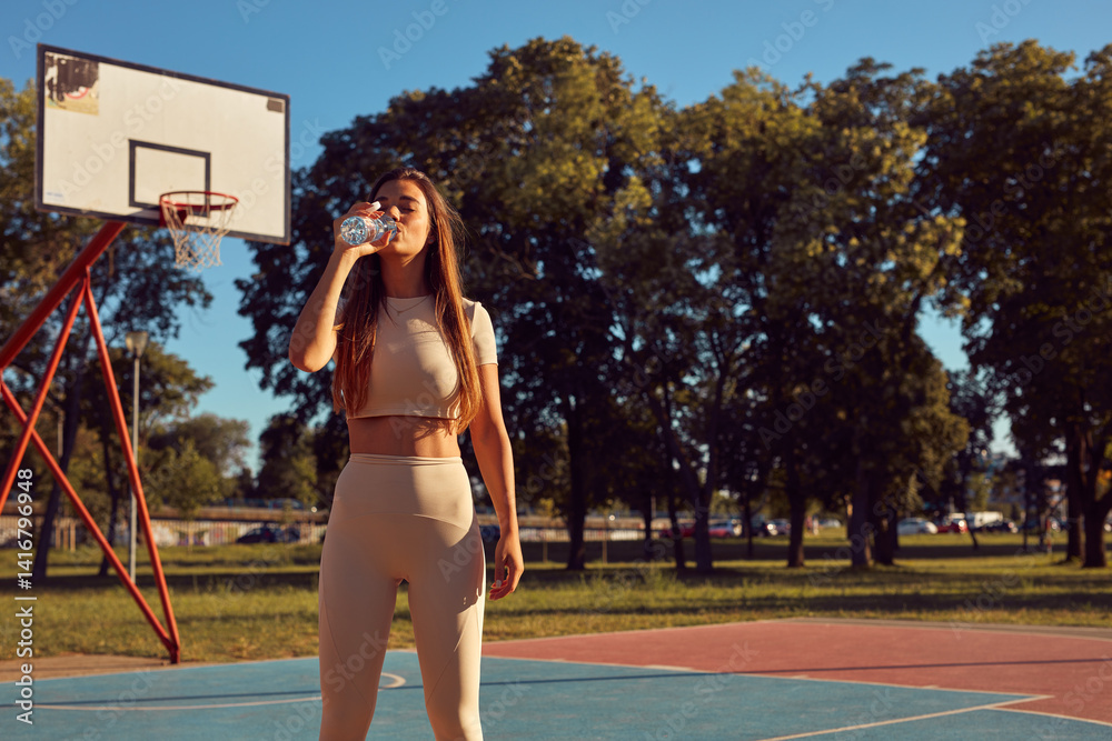 Young woman drinking water after jogging and exercise in urban park.