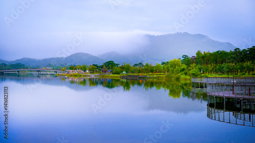 Sejong City, South Korea autumn green space landscape with a hilltop traditional pavilion and reflections over a foggy pond at the National Sejong Arboretum on a rainy morning.