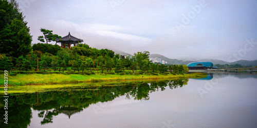 Photography Tranquil autumn landscape at the Sejong National Arboretum in Sejong City, South Korea, with mirror-like reflections on the pond and a hilltop traditional pavilion
