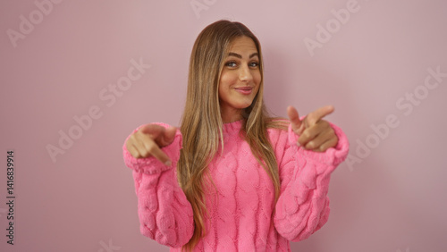 Foto Woman pointing at camera with a playful expression, wearing a pink sweater, on a pink isolated wall background, exuding youthful and attractive vibes for modern lifestyle themes