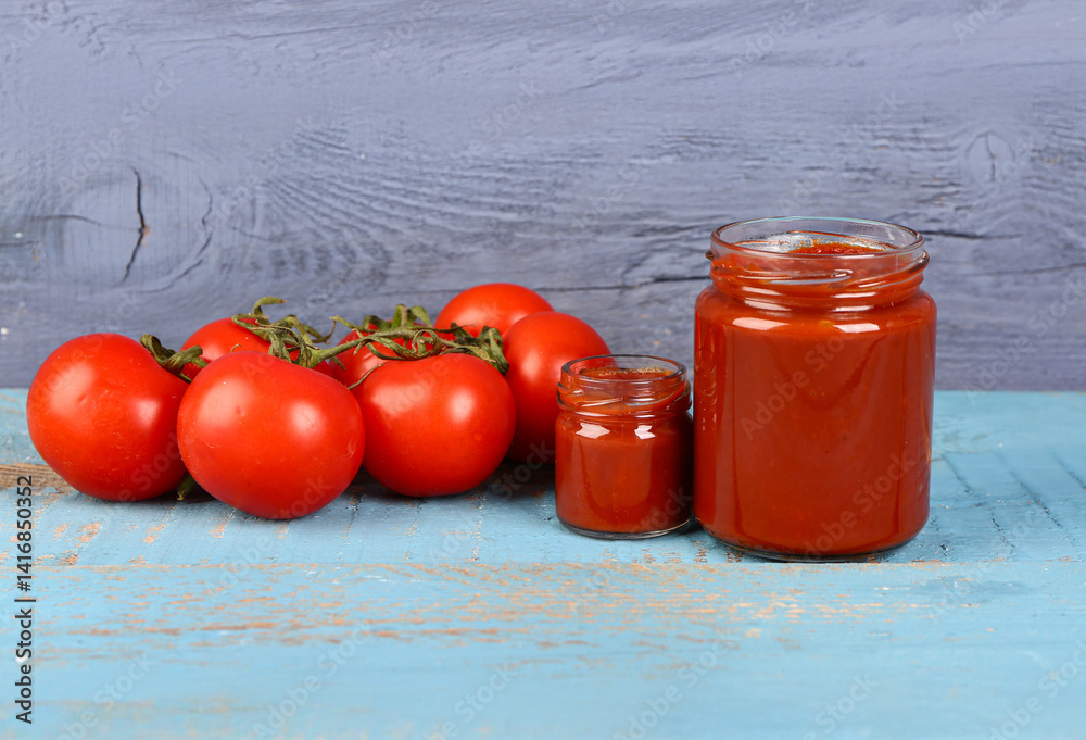 Jars with tasty tomato paste and fresh vegetables on blue wooden background