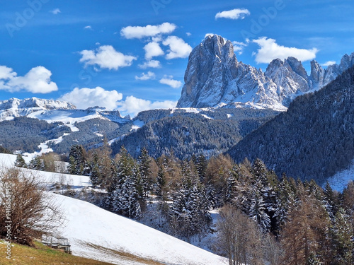 View of the Dolomites in Ortisei in winter. Mount Langkofel in snow in Santa Cristina against a clear blue sky and white clouds. photo