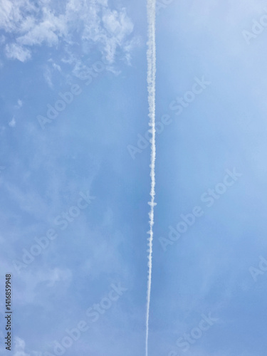 A jet contrail stretches against a partly cloudy sky.