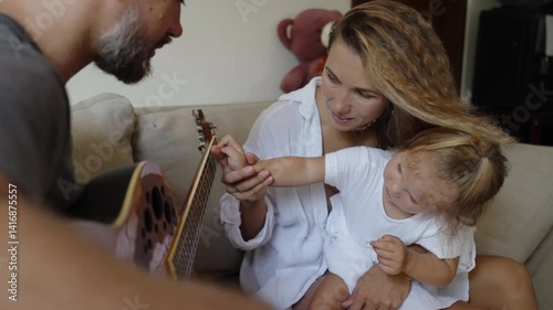 Small girl daughter listening her father playing guitar. Loving dad singing and playing music for his child and wife. Tender family moment of home activity together, mother with daughter with father