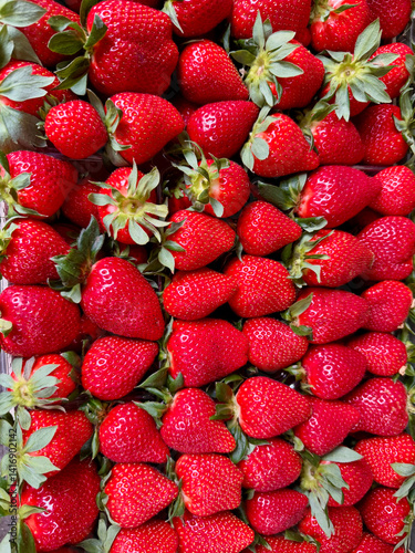 Close-up view of a tightly accurate packed pile of fresh, vibrant red strawberries, displayed on a market stall, ideal for food and freshness concepts