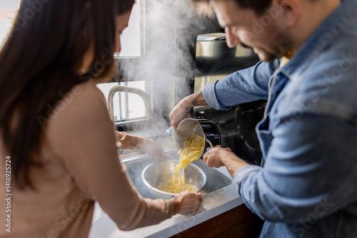 Billede på lærred Man and woman draining steaming hot pasta in a colander, enjoying a moment of te