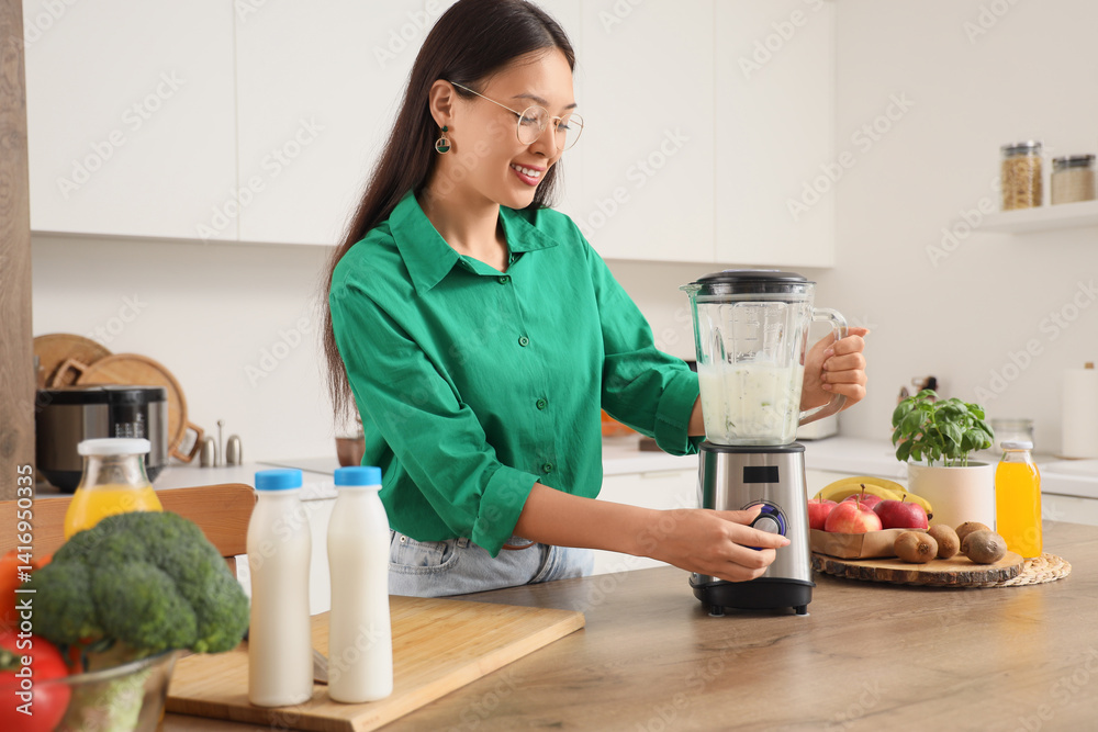 Young Asian woman making smoothie with blender in kitchen