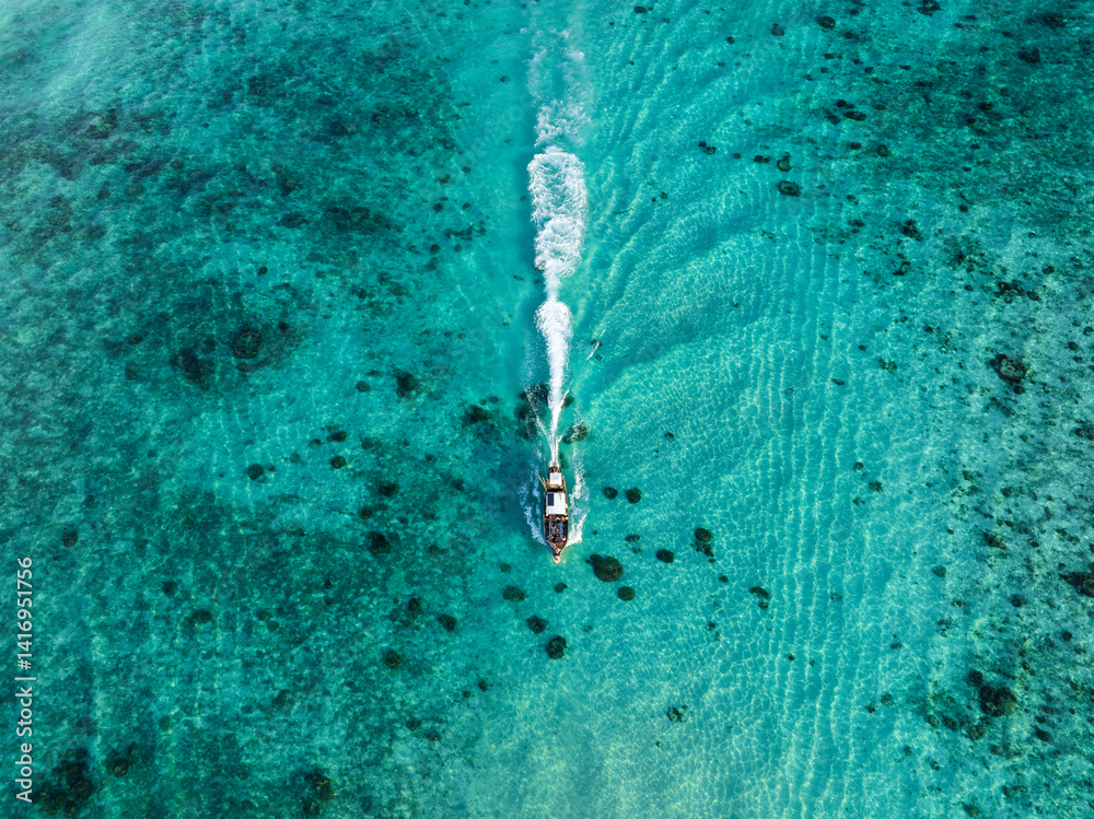 Boat cruising through turquoise waters with white wake trailing behind, captured from directly above in Thailand.