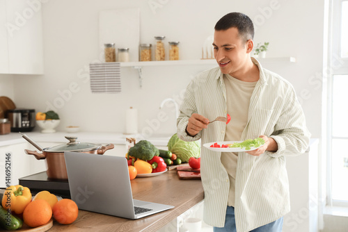 Young man with laptop eatin...