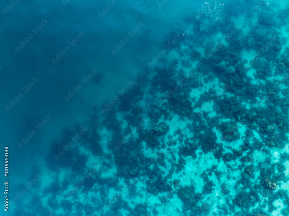 Aerial view of a coral reef beneath turquoise waters, revealing abstract marine textures and vibrant underwater patterns off the coast of Thailand.